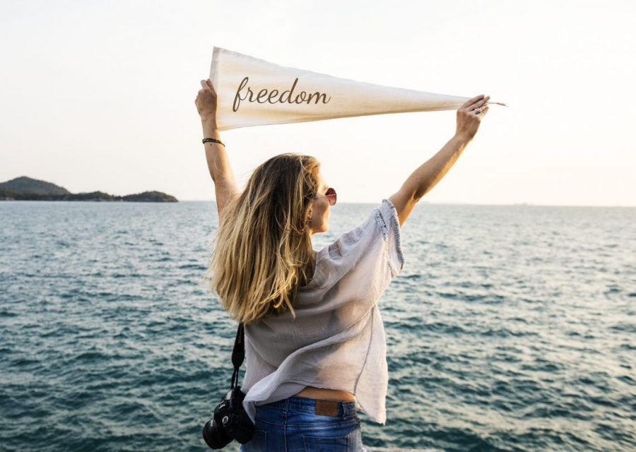 Mujer con frente al mar, sosteniendo una bandera de libertad.